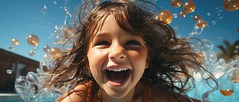 Ein fröhliches und lachendes Mädchen planscht im Swimmingpool in einem Familienhotel und macht ein Selfie mit dem Handy.