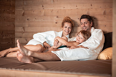 Familie mit Kind liegt gemütlich und entspannt im Bademantel auf einer Liege im Wellnessbereich des Hotels Family Home Alpenhof.